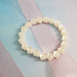 May include: A white flower-shaped beaded bracelet on a pink and blue background.