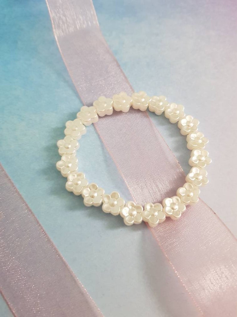 May include: A white flower-shaped beaded bracelet on a pink and blue background.