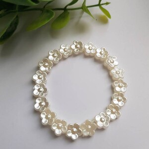 May include: A white flower bracelet made of plastic beads. Each bead is shaped like a flower with five petals.