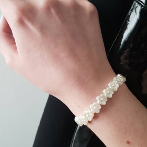 May include: A white flower-shaped beaded bracelet. The bracelet is made of small, white, plastic flowers that are strung together on a clear elastic cord.