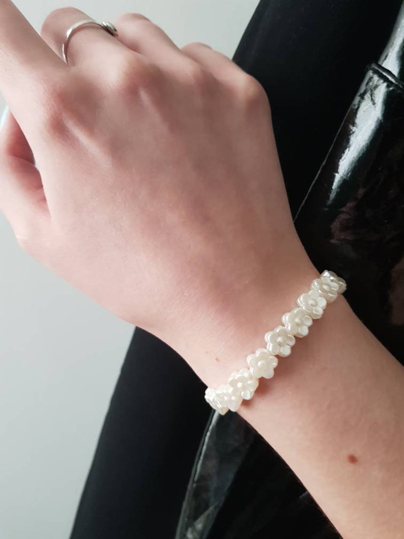 May include: A white flower-shaped beaded bracelet. The bracelet is made of small, white, plastic flowers that are strung together on a clear elastic cord.