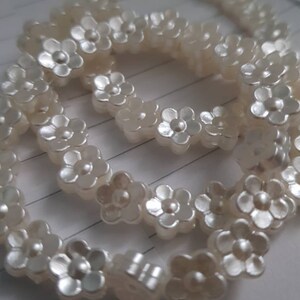 May include: A white pearl necklace with flower-shaped beads. The necklace is made of multiple strands of pearls and is arranged in a circular shape.