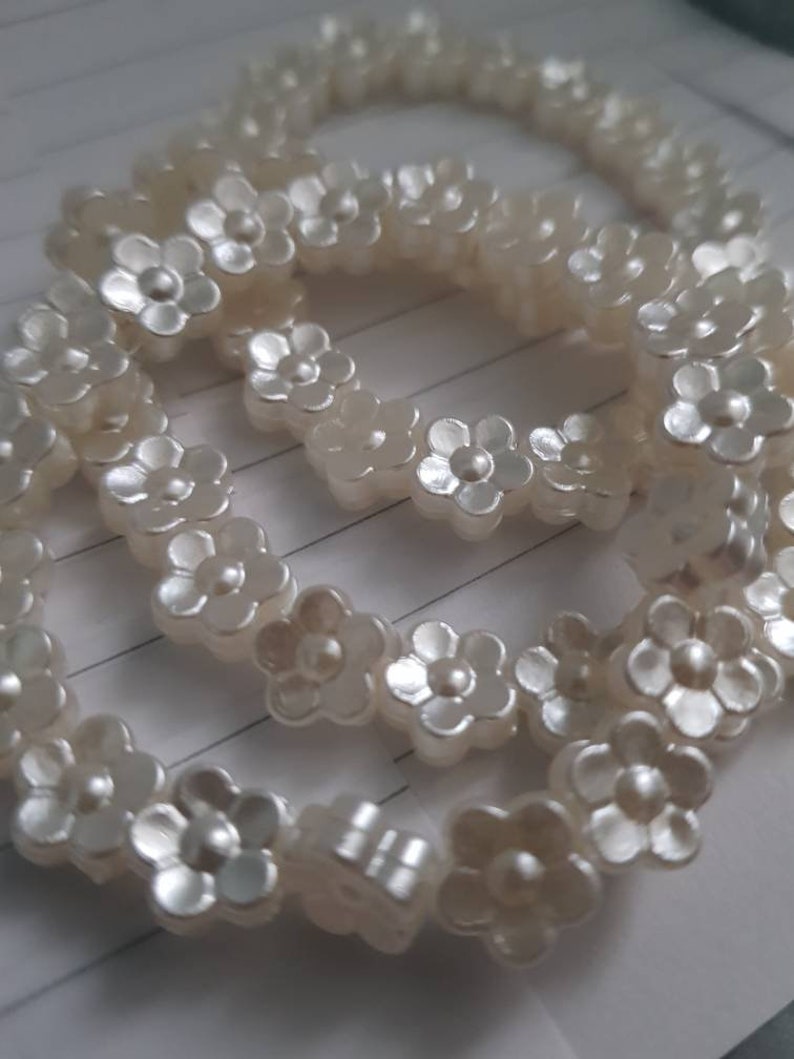 May include: A white pearl necklace with flower-shaped beads. The necklace is made of multiple strands of pearls and is arranged in a circular shape.
