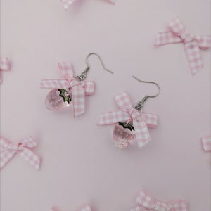May include: A pair of silver earrings with pink gingham bows and clear strawberry charms.