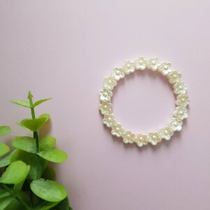 May include: A white flower-shaped beaded bracelet on a pink background.
