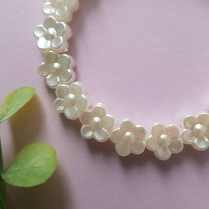 May include: A white pearl flower bracelet with a delicate design. The bracelet is made of small, white pearl flowers that are strung together on a clear elastic cord.