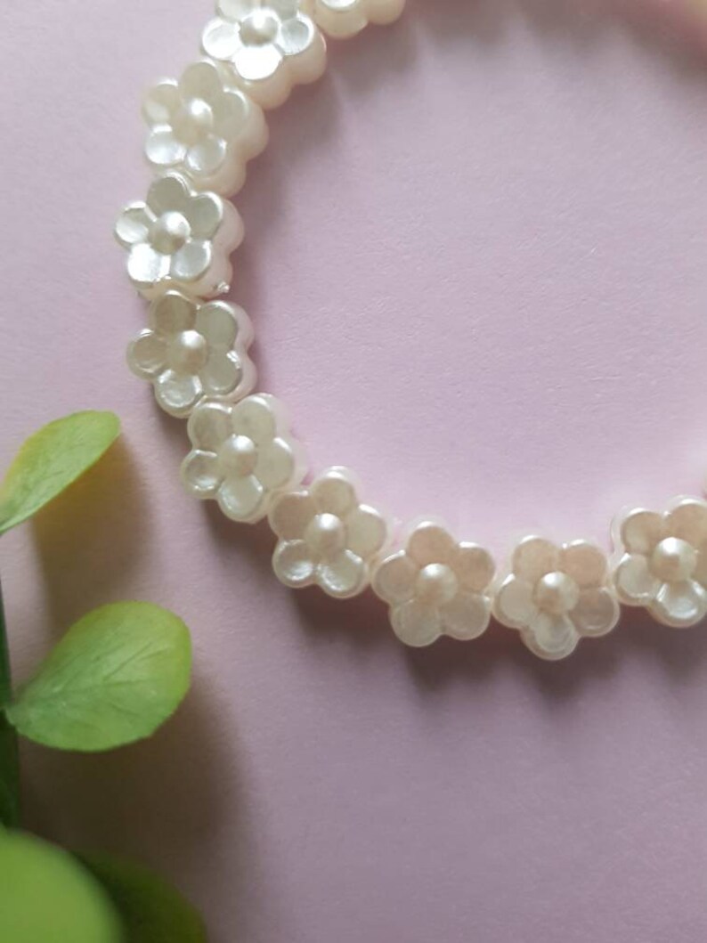 May include: A white pearl flower bracelet with a delicate design. The bracelet is made of small, white pearl flowers that are strung together on a clear elastic cord.