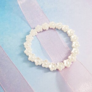 May include: A white flower-shaped beaded bracelet on a light blue and purple background.