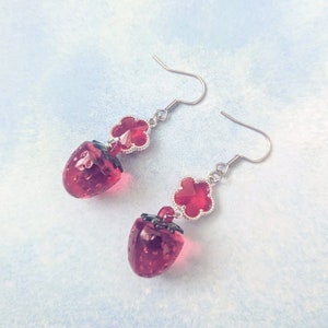 Peut inclure: Une paire de boucles d'oreilles pendantes avec un charme de fraise rouge et un charme de fleur en cristal rouge. Les boucles d'oreilles sont en m&eacute;tal argent&eacute;.