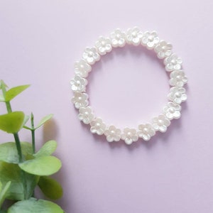 May include: A white flower-shaped beaded bracelet on a light pink background.