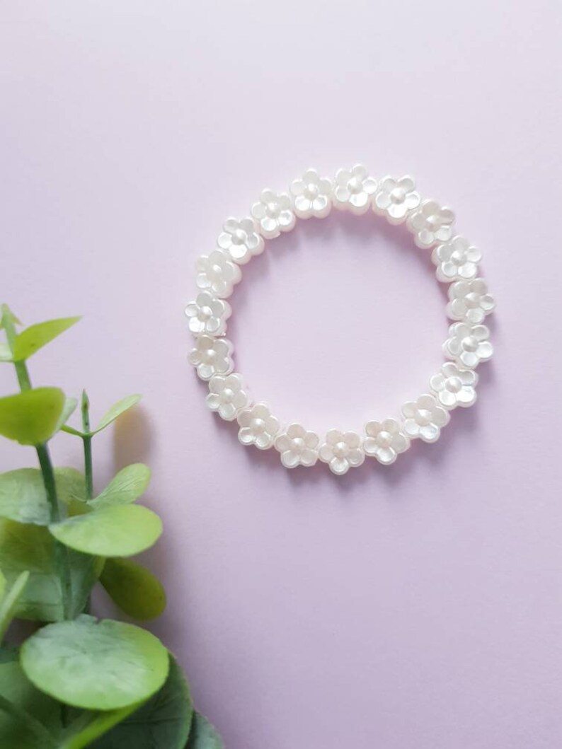 May include: A white flower-shaped beaded bracelet on a light pink background.