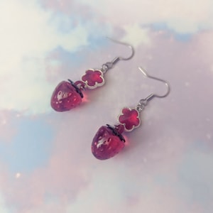 Peut inclure: Une paire de boucles d'oreilles pendantes avec un charme en forme de fraise en verre rouge et un charme en forme de fleur en verre rouge sur un crochet argent&eacute;.