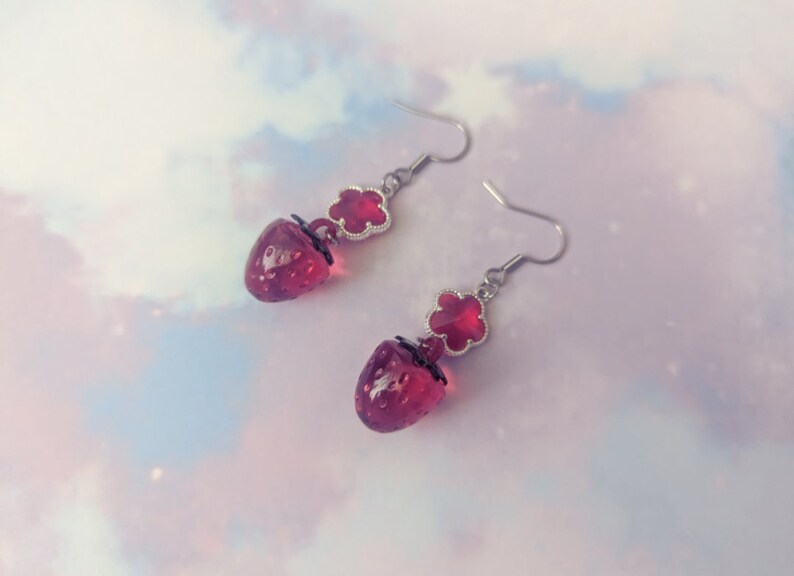 Peut inclure: Une paire de boucles d'oreilles pendantes avec un charme en forme de fraise en verre rouge et un charme en forme de fleur en verre rouge sur un crochet argent&eacute;.