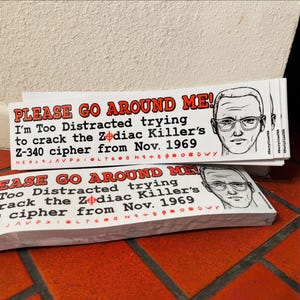 May include: A stack of white bumper stickers with the text "PLEASE GO AROUND ME!" in red, along with the phrase "I'm Too Distracted trying to crack the Zodiac Killer's Z-340 cipher from Nov. 1969." A black and white illustration of a man with glasses is on the right.