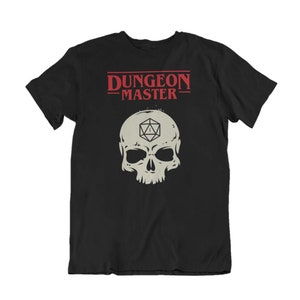 Könnte beinhalten: Schwarzes T-Shirt mit einem weißen Totenkopf und einem roten "Dungeon Master"-Aufdruck. Der Schädel hat einen 20-seitigen Würfel im Auge.
