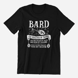 Può includere: Maglietta nera con testo bianco che recita "BARD THE MASTER OF SONG I AM THE TELLER OF TALES AND HERO OF TAVERNS STORIES ARE MORE POWERFUL THAN ANY WEAPON". Il testo è circondato da note musicali e un'immagine bianca di un liuto.