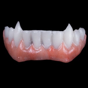 May include: A set of white vampire teeth with a pink gum line. The teeth are pointed and sharp, and the gum line is realistic.