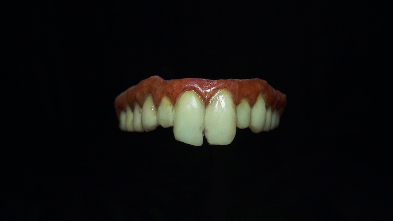 May include: A set of fake teeth with a red gum line and yellow teeth. The teeth are slightly crooked and have a chipped front tooth.