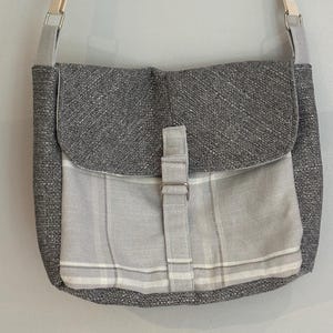 May include: A grey and white canvas crossbody bag with a flap closure and a buckle. The bag has a plaid pattern on the front flap.