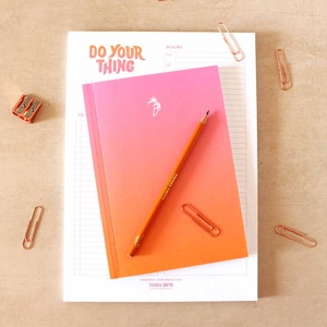 May include: A white notepad with a pink and orange gradient notebook on top. The notepad has the text "DO YOUR THING" in a retro font. The notebook has a palm tree logo and the text "PROGRESS OVER PERFECTION TINARA SMITH".
