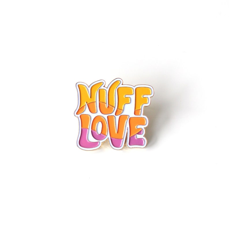 K&ouml;nnte beinhalten: Eine goldfarbene Emaille-Anstecknadel mit den Worten "Nuff Love" in einer retro-stilisierten Schrift. Die Buchstaben sind mit orangefarbenem und rosafarbenem Email gef&uuml;llt.