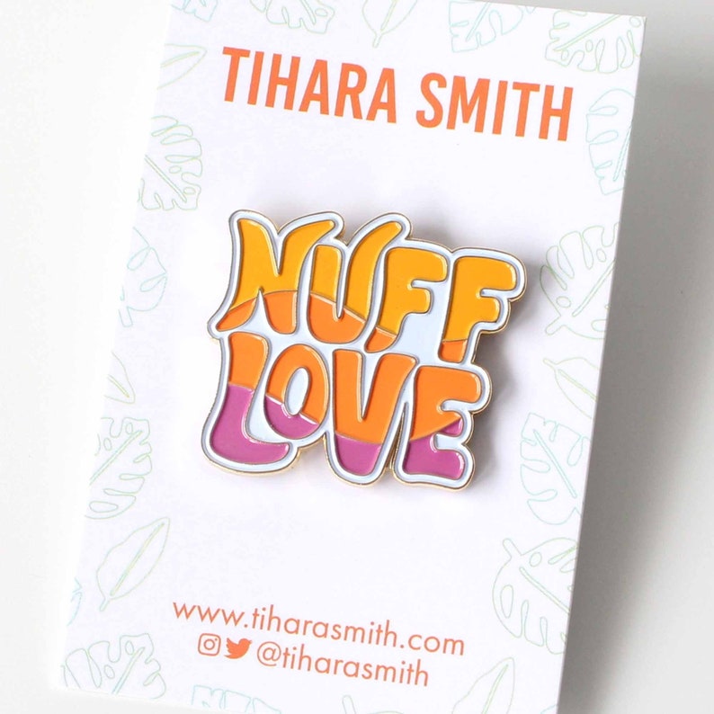 K&ouml;nnte beinhalten: Eine goldfarbene Emaille-Anstecknadel mit den Worten "Nuff Love" in einer Retro-Schriftart. Die Buchstaben sind in Orange, Gelb und Rosa &uuml;bereinander gelegt.