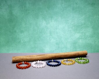May include: Six colorful beaded bracelets with silver clasps. The bracelets are arranged in a row on a gray surface. The bracelets are red, pink, blue, yellow, and green.