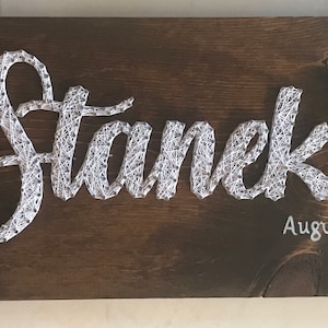 Può includere: Un cartello in legno marrone con il testo "The Stanek's" in arte di filo bianco. La data "August 31, 2019" è anche scritta in arte di filo bianco.