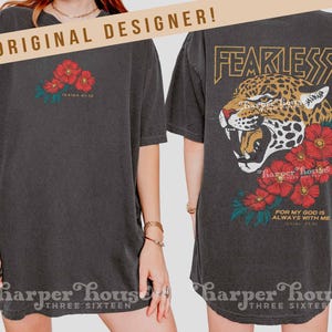 Puede incluir: Camiseta gris oscuro con un diseño floral y el texto "Isaías 41:10" en la parte delantera. La parte trasera presenta un gráfico de leopardo con la palabra "FEARLESS" y el texto "FOR MY GOD IS ALWAYS WITH ME Isaías 41:10".