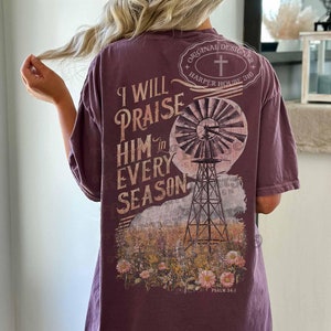 May include: A purple t-shirt with a vintage-style graphic of a windmill and the text "I will praise him in every season" and "Psalm 34:1".