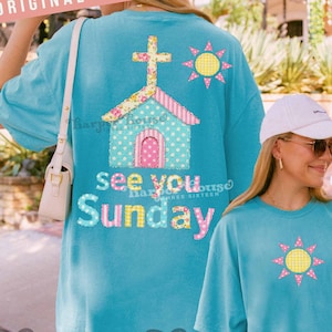 Peut inclure: T-shirt bleu turquoise avec un motif d'église et de soleil. L'église a une croix, un toit floral et des murs à pois. Le texte sur le t-shirt dit "See You Sunday". Le t-shirt est ample et confortable.
