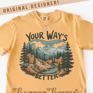 May include: Mustard yellow t-shirt with a mountain and river graphic. The graphic includes the text "Your Way's Better" and "Harper House Three Sixteen". The shirt has short sleeves and a crew neck.