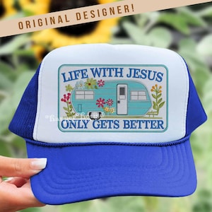 May include: A blue and white trucker hat with a blue peak and mesh back. The front panel displays a turquoise camper illustration with the text "LIFE WITH JESUS ONLY GETS BETTER" in a rectangular frame. The hat has the text "ORIGINAL DESIGNER!" at the top.