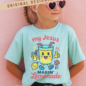 Op de afbeelding: Een lichtblauw t-shirt met de tekst "my Jesus MAKIN' Lemonade" en een cartoon limonade karakter. Het shirt heeft ook een kleine citroen, een bloem en de tekst "Harper House THREE SIXTEEN".