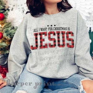 May include: Gray sweatshirt with a red and black buffalo plaid design. The text "All I want for Christmas is Jesus" is printed on the front of the sweatshirt.