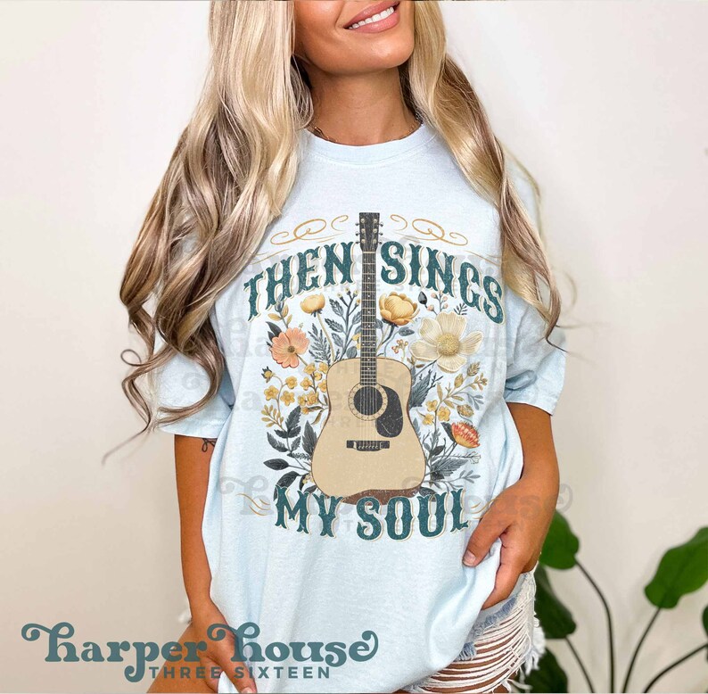 May include: A light blue t-shirt with a floral design featuring a guitar and the text "Then Sings My Soul".
