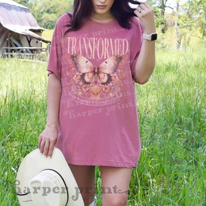 May include: A pink oversized t-shirt with a butterfly graphic and the text "TRANSFORMED" and "BE TRANSFORMED BY THE RENEWING OF YOUR MIND".