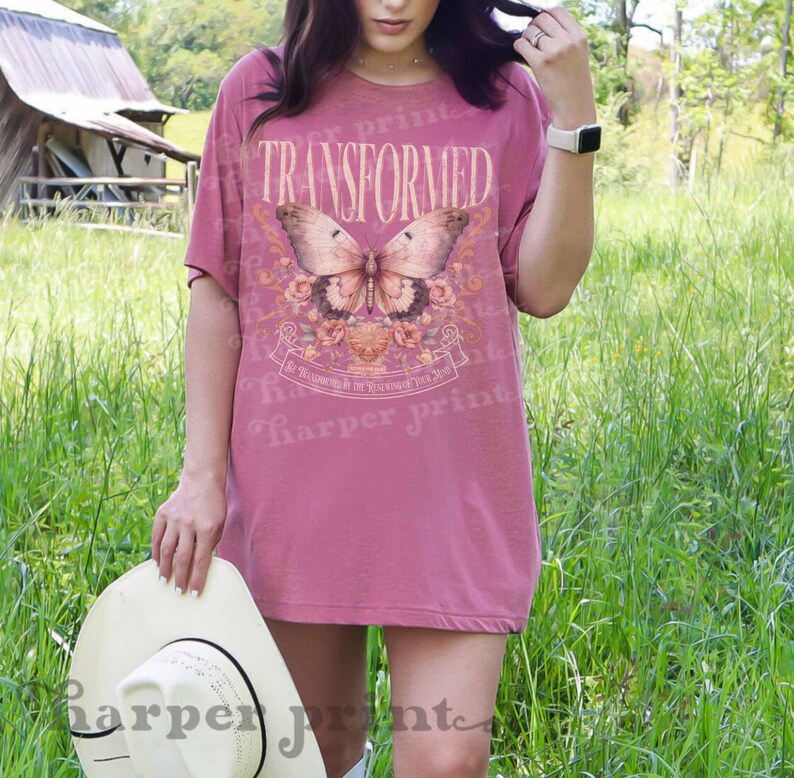 May include: A pink oversized t-shirt with a butterfly graphic and the text "TRANSFORMED" and "BE TRANSFORMED BY THE RENEWING OF YOUR MIND".