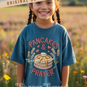 May include: Teal t-shirt with embroidered text and design. The design features the words "PANCAKES & PRAYER" with a stack of pancakes, hearts, and floral elements. The shirt is from Harper House Three Sixteen.