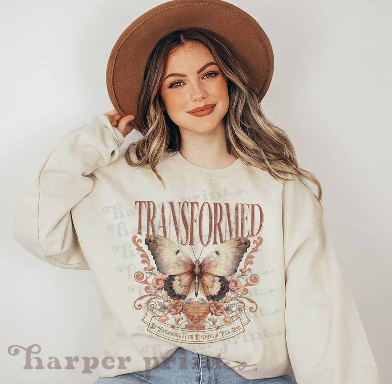 May include: A cream-colored sweatshirt with a graphic print of a butterfly with pink flowers and the word "TRANSFORMED" in red. The text below the butterfly reads "Be transformed by the renewing of your mind."