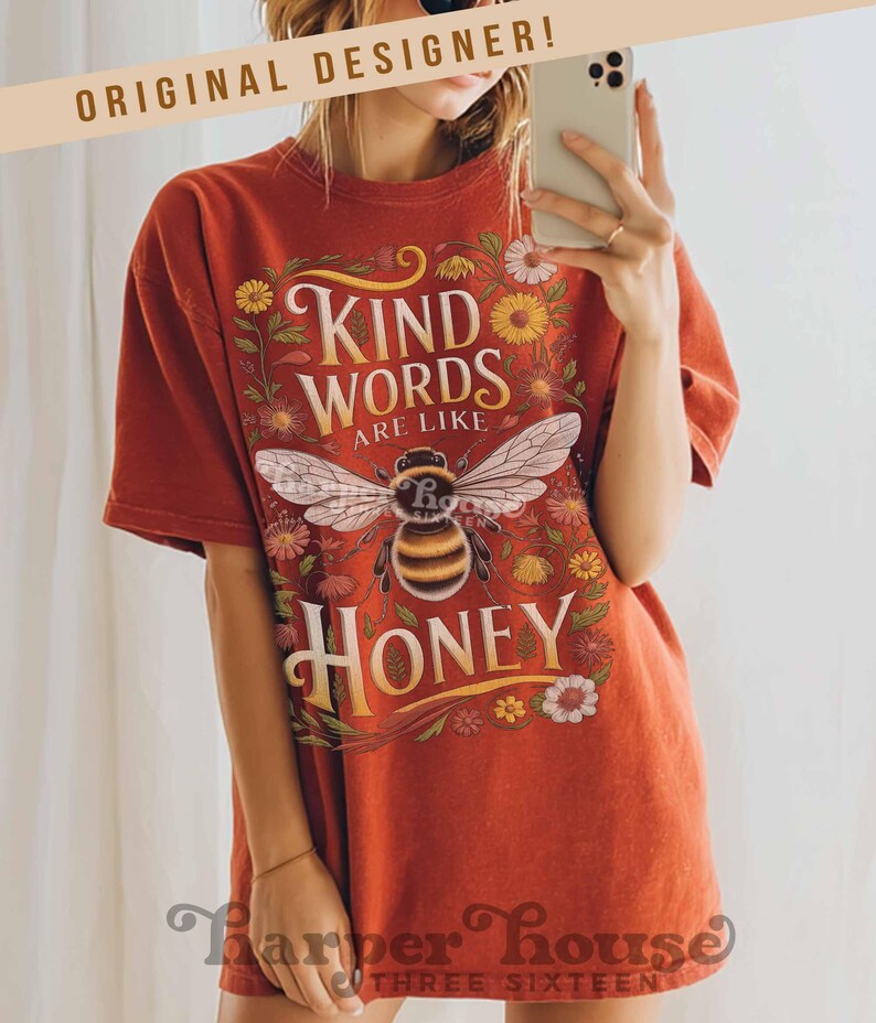 Peut inclure: T-shirt rouille avec un motif d'abeille et les mots "Kind Words Are Like Honey". Le graphisme comprend des &eacute;l&eacute;ments floraux. Le t-shirt a des manches courtes et une coupe d&eacute;contract&eacute;e.