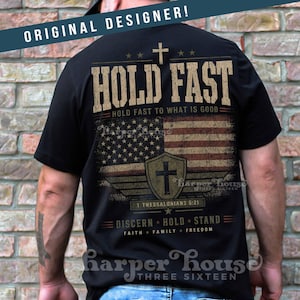 May include: Black t-shirt with a distressed American flag design and the words "HOLD FAST" and "DISCERN HOLD STAND". The shirt also features a cross and the text "1 THESSALONIANS 5:21".
