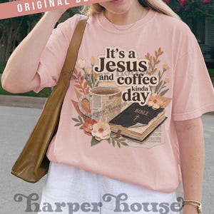 May include: A light pink t-shirt with the text "It's a Jesus and coffee kinda day." The graphic includes a coffee cup, a Bible, and floral accents. The words "Original Designer" are at the top.