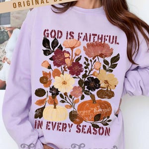 May include: A light purple sweatshirt featuring a floral design with pumpkins and the text "GOD IS FAITHFUL IN EVERY SEASON." The design includes flowers in shades of burgundy, orange, and cream. The brand name "Harper House" is also visible.