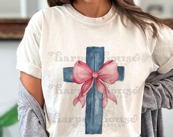Peut inclure: Un t-shirt à manches courtes de couleur crème avec un motif de croix bleue style aquarelle centré sur la poitrine. Un grand nœud rose tendre est noué au milieu de la croix. Le texte Harper House est répété légèrement en arrière-plan.