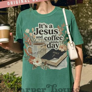 May include: Green t-shirt with the phrase "It's a Jesus and coffee kinda day" printed on the front. The graphic includes a coffee cup, a Bible, and floral accents. The shirt is a comfortable, casual style.