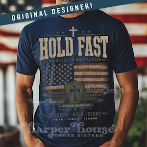 May include: Navy blue t-shirt with a distressed American flag design and the words "HOLD FAST." The shirt includes a cross, stars, and the text "HOLD FAST TO WHAT IS GOOD." Additional text includes "1 Thessalonians 5:21" and "DISCERN HOLD STAND FAITH FAMILY FREEDOM."