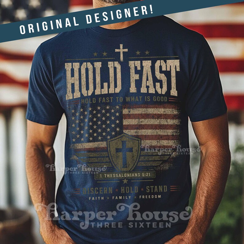 May include: Navy blue t-shirt with a distressed American flag design and the words "HOLD FAST." The shirt includes a cross, stars, and the text "HOLD FAST TO WHAT IS GOOD." Additional text includes "1 Thessalonians 5:21" and "DISCERN HOLD STAND FAITH FAMILY FREEDOM."