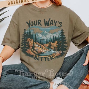May include: Olive green t-shirt with a mountain and forest graphic. The graphic includes the text "Your Way's Better" in a stylized font. The shirt is a relaxed fit and has short sleeves.