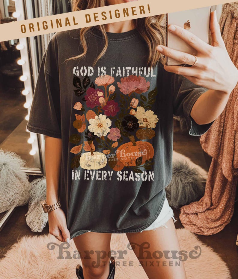 May include: Dark gray t-shirt with a floral and pumpkin graphic. The design includes the text "GOD IS FAITHFUL" and "IN EVERY SEASON". The shirt also features the text "harper house THREE SIXTEEN" at the bottom.